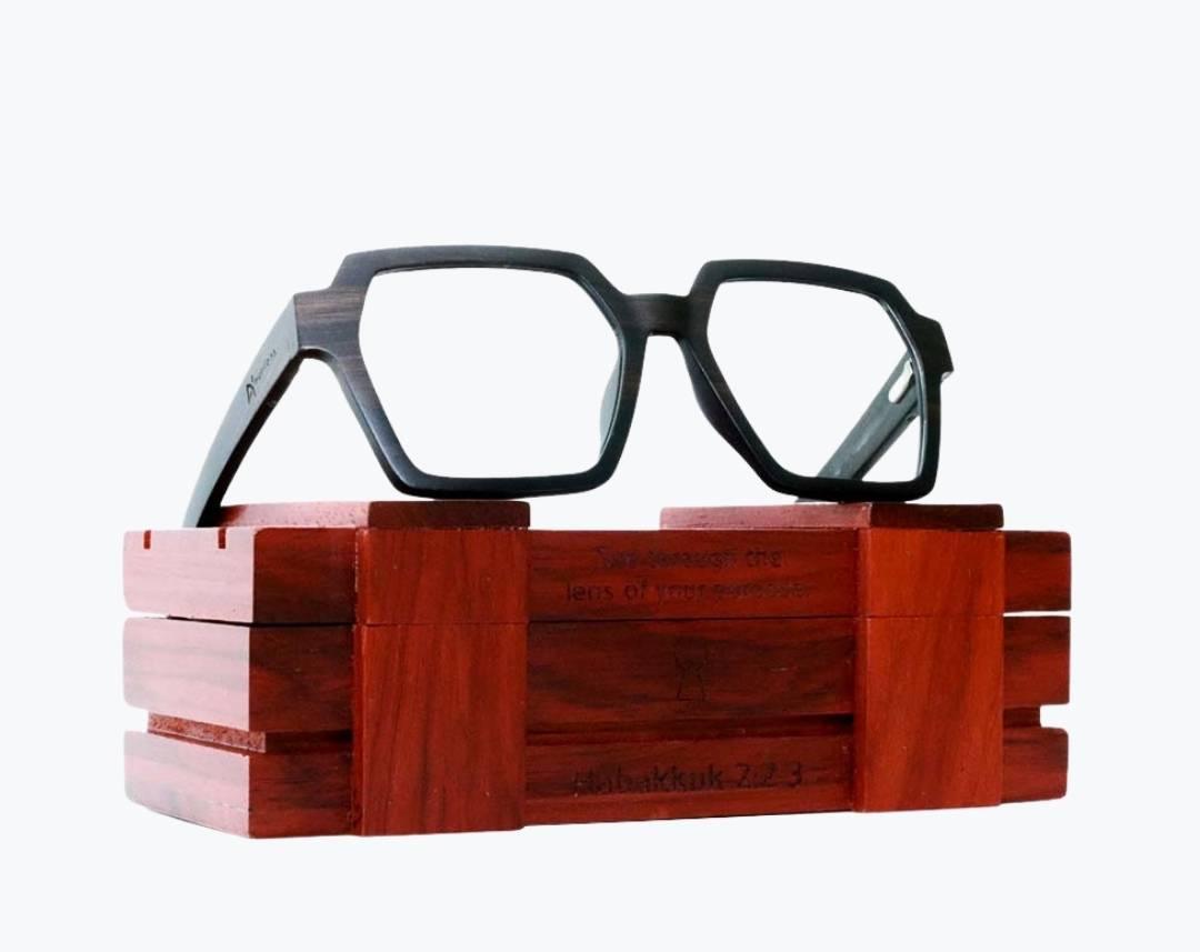 Dark brown wayframe eyeglasses made of ebony with subtle black wood grain sitting on rosewood wooden case by NURILENS.