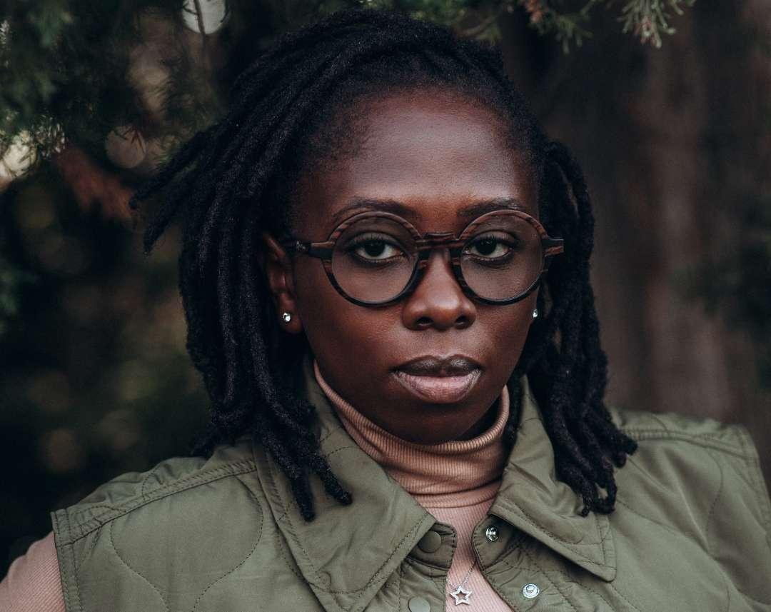 Black woman with short dreadlocks wearing round wooden glasses made of ebony with subtle black wood grain by NURILENS.
