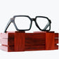 Dark brown wayframe eyeglasses made of ebony with subtle black wood grain sitting on rosewood wooden case by NURILENS.