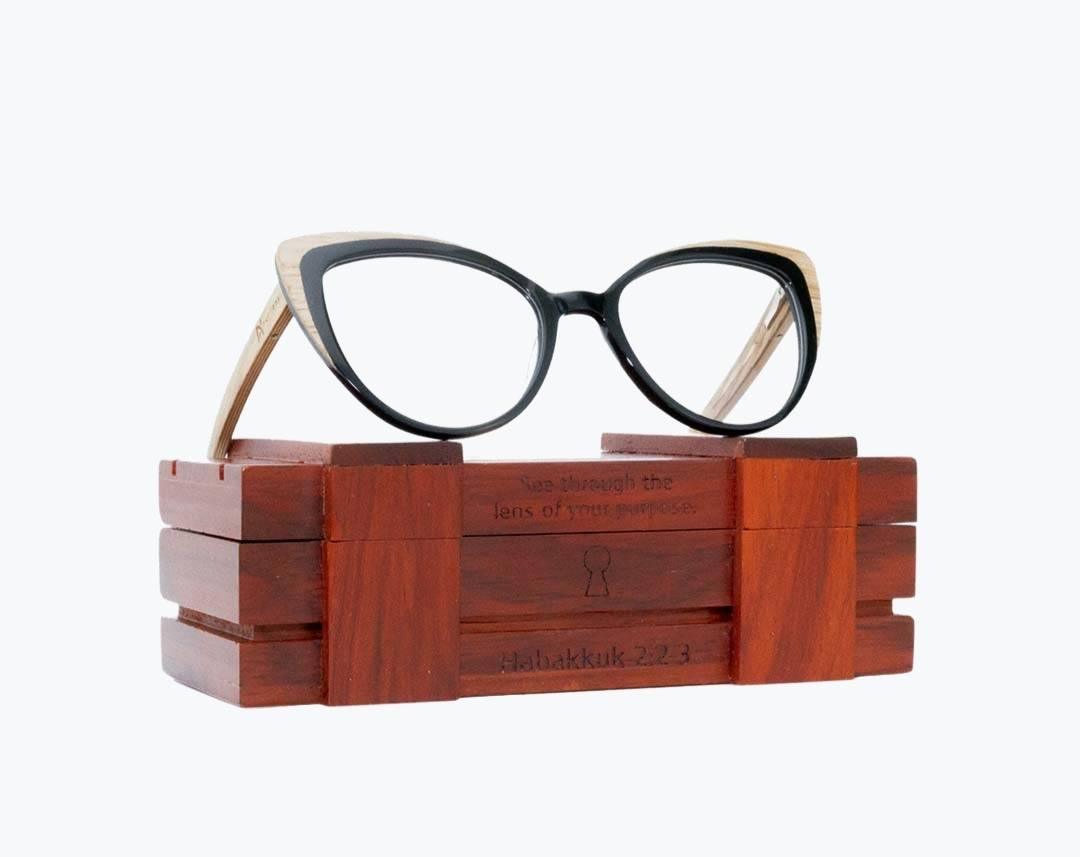 Wooden cat eye eyeglasses made of light brown oak and black acetate sitting on rosewood wooden case by NURILENS.