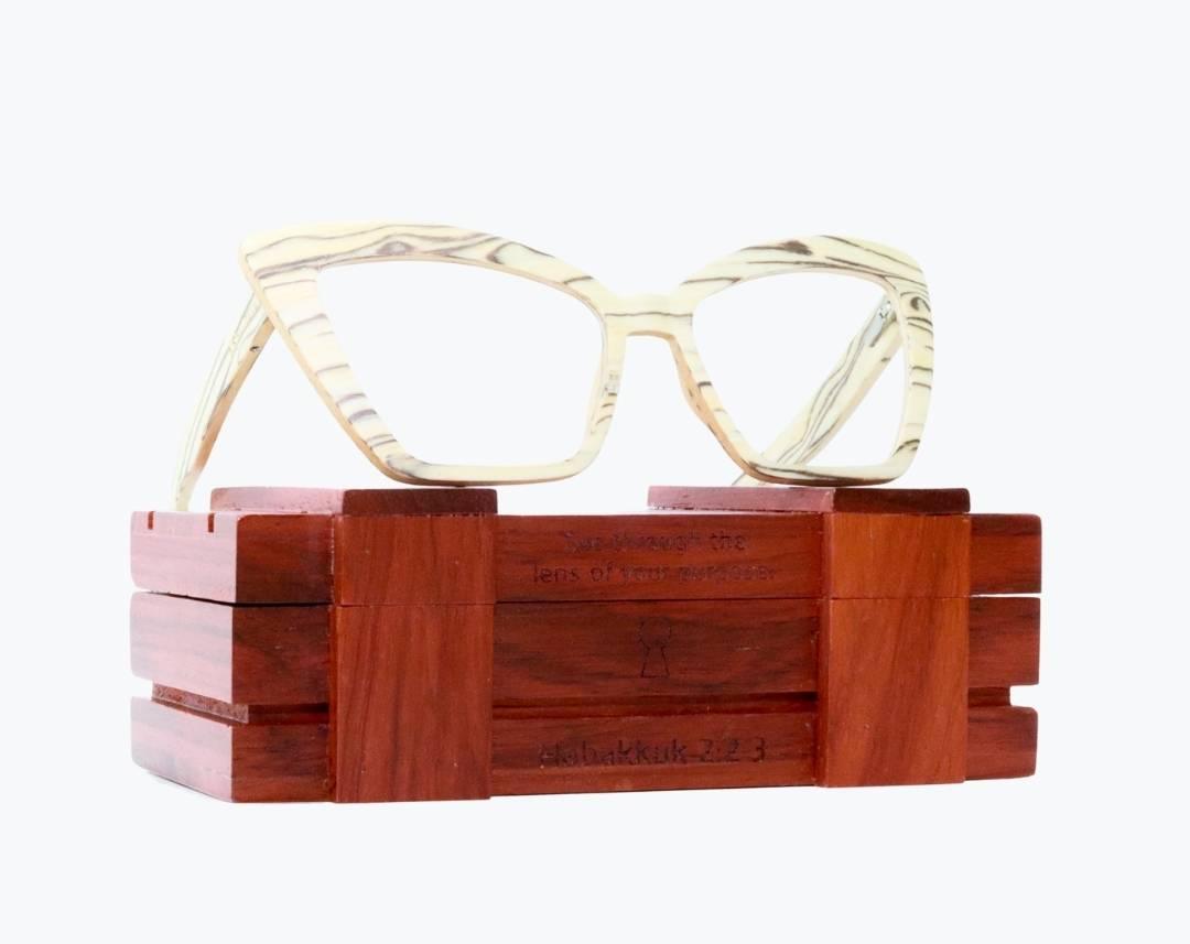 Beige cat eye wooden eyeglasses made of ice wood with black striped wood grain accents sitting on rosewood wooden case by NURILENS.