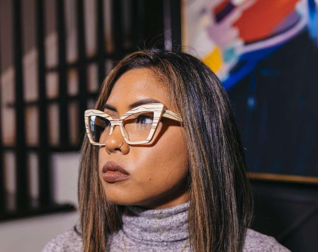 Hispanic woman wearing beige cat eye wooden eyeglasses made of ice wood with black striped wood grain accents by NURILENS.