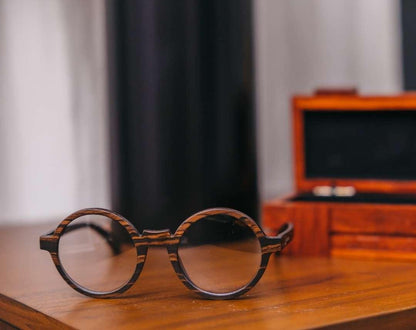 Round wooden glasses made of ebony with subtle black wood grain by NURILENS in front of wooden case.